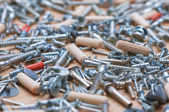 Pile of mixed furniture assembly hardware with screws, dowels and fasteners on wooden surface. Hardware store and furniture manufacturing guides.