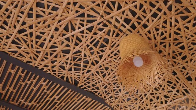 Intricate woven bamboo ceiling design with a hanging lamp fixture.