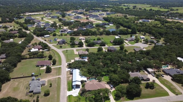 Custom homes feature broad lawns, metal accessory buildings along County Road 602 in Dallas Fort Worth. Broad aerial view captures winding road paths spanning housing developments. Burleson, TX