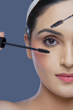 Cropped image of pretty young woman with mascara and eyebrow tinting applicator over colored background 