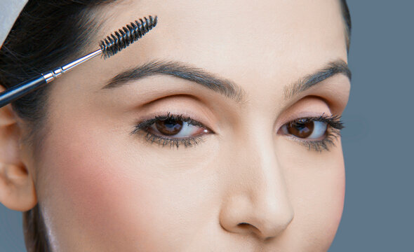 Close-up of young female with eyebrow tinting applicator over colored background 
