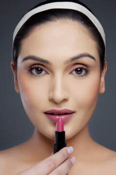 Portrait of a beautiful young woman holding lipstick over colored background 