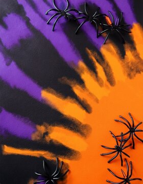 Top view of halloween tie and dye black, purple and orange background with purple spiders and lateral copy space