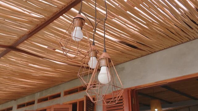 Modern industrial pendant lights hanging from a rustic bamboo ceiling in a cozy interior.