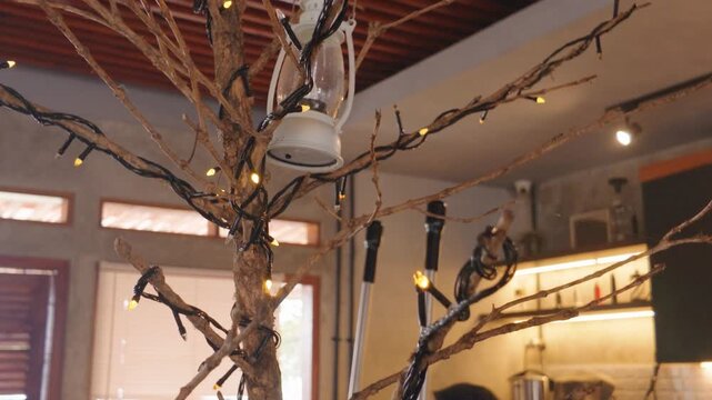 Decorated indoor decorative tree with fairy lights and hanging vintage lantern in cafe interior.