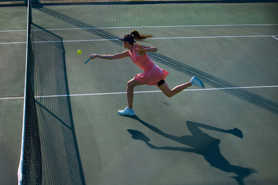 Female player sprinting forward for low pickleball return. Concept of summer sport cardio, footwork drills, fitness coaching and active recreation advertising.