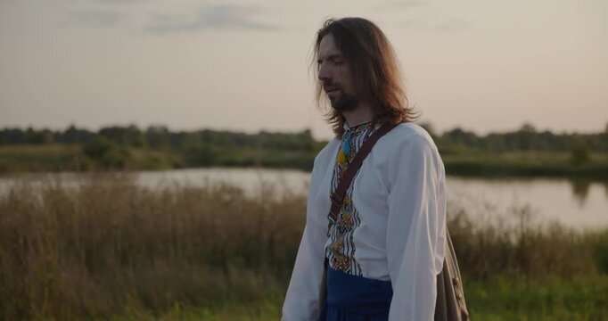 Caucasian man with long hair and Ukrainian traditional folk attire walk wandering on nature. 4K 10-bit