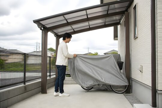 カーポートで自転車にカバーをかける男性
