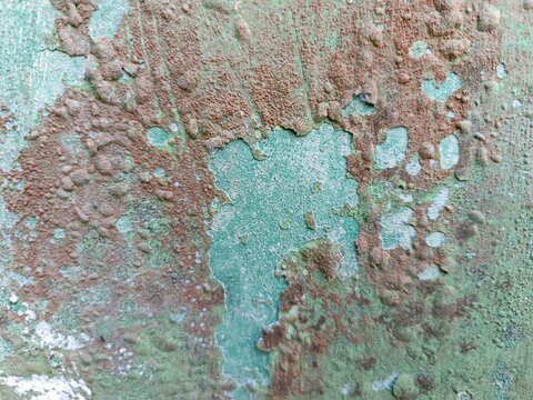 oA texture of a weathered and corroded surface with peeling green paint, revealing a rough, rusty brown underlayer, bubbly paint blisters, heavily oxidized metal, rustic industrial decay, and a gritty