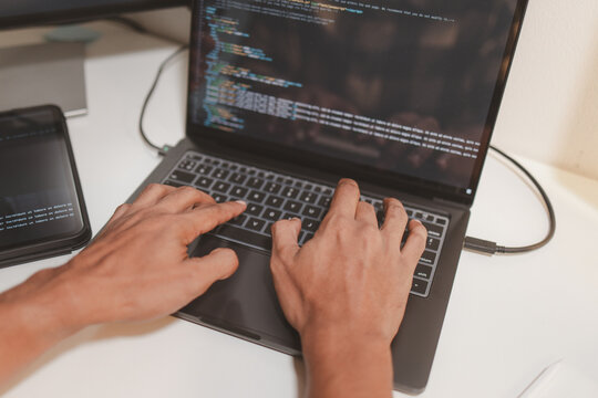 Software developer coding with laptop, tablet, and dual monitors displaying source code. Modern programming workspace representing software development, debugging, technology, and remote work.