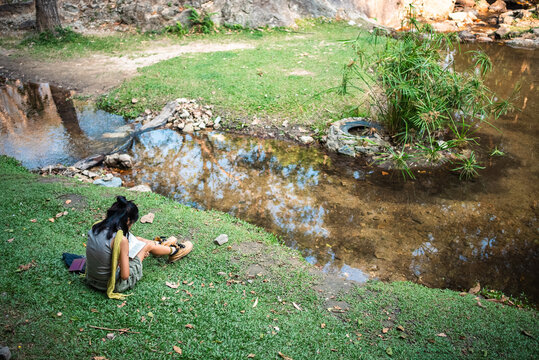 Young woman reading novel book and writing notes by river in peaceful nature, teenage girl studying and reflecting in calm solitude outdoors near water, calm lifestyle scene