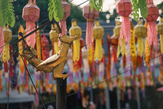 Buddhist temple ritual hanging bird figurine for pouring water to Buddha statue, shrine merit ceremony with rope pulley and sacred offering, colourful Asian lanterns, Chiang Mai, Thailand