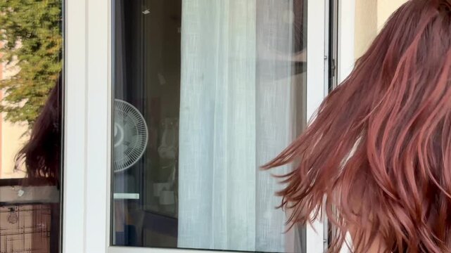 Red haired Gen Z teenager dances emotionally with hair flying beside window reflection in slow motion 4K. Concept of dynamic self expression captured through silhouette in cinematic video clip.