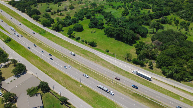 Multilane transit stretches alongside South Blvd Interstate 35W in Dallas Fort Worth suburbs. Moving vehicles, freight trucks traverse paved lanes bordered by green pastures, Burleson, TX