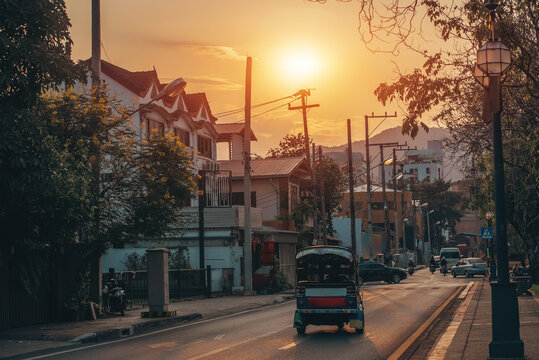 traditional tuk tuk driving through Thai city street during golden sunset hour, urban Thailand transportation scene with evening traffic and warm tropical cityscape background