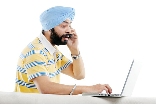 Sikh man talking on the phone while working on a laptop 