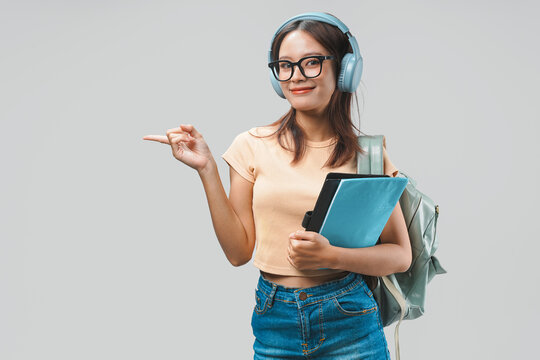 Young Asian college student is pointing to the copy space beside her.