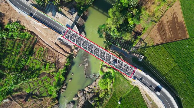 Aerial view of Jembatan Sidabowa crossing a river surrounded by lush green rice fields and rural landscape in Kecamatan Patikraja, Jawa Tengah, Indonesia.