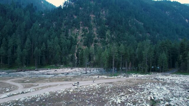 Rocky riverbed borders a dense cedar forest at the base of mountain slopes, Upper Dir District, Khyber Pakhtunkhwa, Pakistan