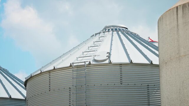Static shot of a modern grain silo top with shiny galvanized steel construction against a bright blue summer sky