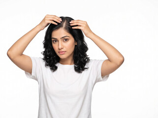 Fototapeta premium Young Indian woman gently separating crown hair to inspect scalp and early thinning for hair loss awareness and dermatology care on white background