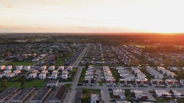 Stunning aerial footage of a spacious modern suburban neighborhood captured at sunset, showcasing rows of contemporary homes, quiet streets, and lush greenery under warm golden light.