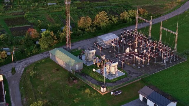 Stunning aerial drone video captures a rural electrical substation amid lush green fields, vibrant vegetation, and winding country roads at golden hour, with dramatic shadows and clear, crisp lighting