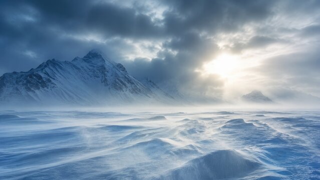 Vast icy landscape with windblown snowdrifts and dramatic sunlit clouds over rugged snow-covered mountains