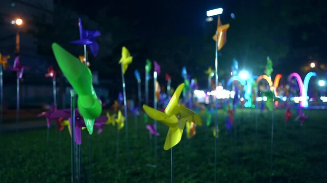 colorful pinwheel decorations glowing at night festival with vibrant bokeh lights, playful spinning windmills in illuminated outdoor park with festive atmosphere background 4k