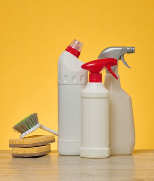 White plastic spray bottle and a stack sponges stand on a wooden surface against a yellow background.
