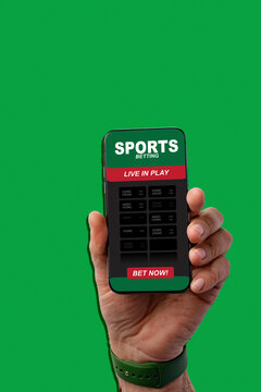 Hand holding smartphone showing sports betting app on green background during live event