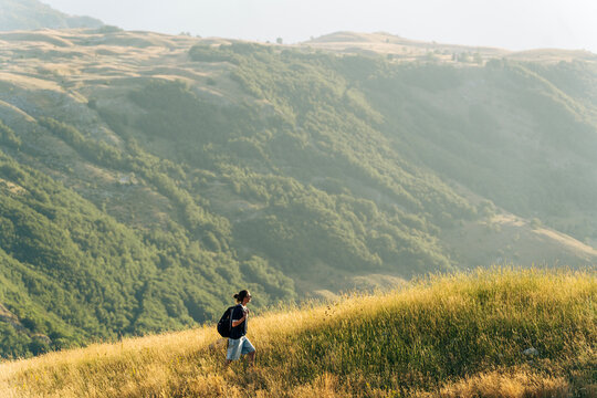 Female traveler walking on green hill slope, admiring epic landscape view. Small person big nature concept