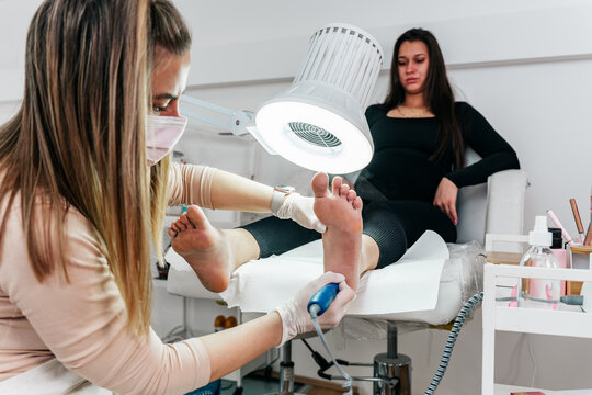 Specialist wearing protective mask and gloves applying antiseptic spray to a client's feet during a clinical podiatry consultation and hygiene treatment.