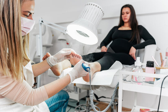 Specialist wearing protective mask and gloves applying antiseptic spray to a client's feet during a clinical podiatry consultation and hygiene treatment.