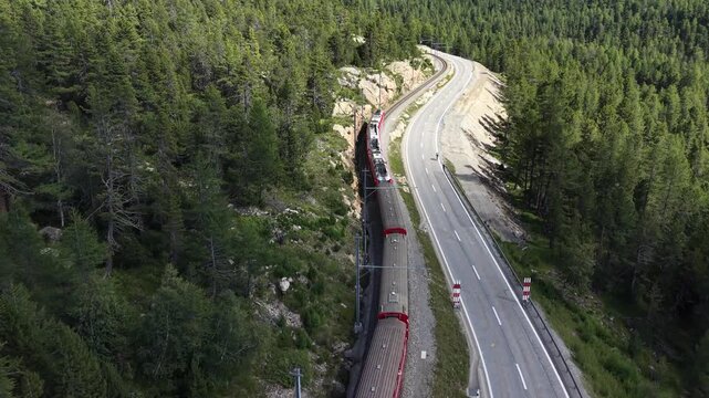 Aerial view of the red Bernina Express train winding through the alpine landscape near Pontresina, Grisons, Switzerland.