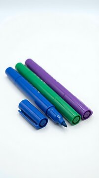 Colorful marker pens arranged in rows featuring blue, green, and purple felt-tip markers with caps on white background for art and design projects.