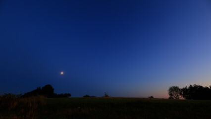 Moon on a twilight sky with stars, planets and landscape mountain silhouettes. © astrosystem