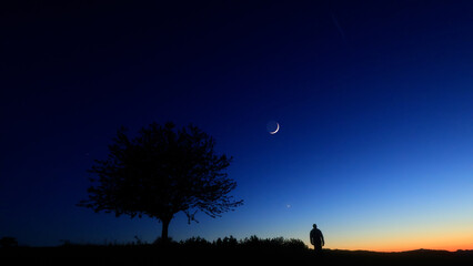Silhouette of a person in nature observing night sky, Moon, stars and planets from a remote location. © astrosystem