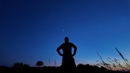 Silhouette of a person in nature observing night sky, Moon, stars and planets from a remote location. © astrosystem
