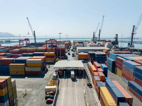 Aerial drone view of a container terminal entrance gate with trucks, port check-in checkpoint, colorful shipping containers, cranes and sea background for global logistics and trade concept.        
