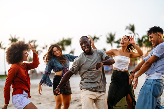 Happy young people embracing the beach lifestyle, dancing barefoot in the sand, celebrating freedom
