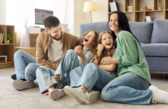 Parents tickling children sisters spark laughter at home. Playful bonding and family happiness as mom and dad sit on the living room floor. Concept of joyful parenting and togetherness