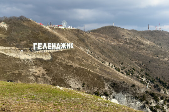 Gelendzhik, Russia - 09.03.2024: Large russian white letters spelling Gelendzhik are positioned on a hillside, with a coastal town visible below. Ferris wheel and various buildings in the background