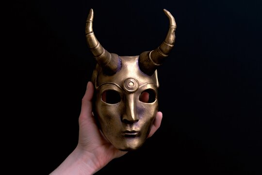 Hand holding golden horned mask with third eye symbol