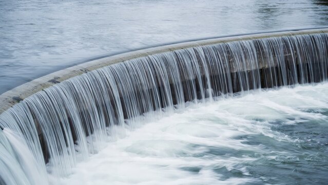 Close up of cascading water over a circular industrial weir dam structure with industrial engineering structure