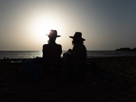 Couple Sitting on Beach at Sunset Facing the Ocean