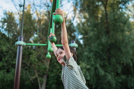 Smiling boy hangs on a playground obstacle course in the park