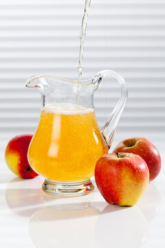 Apple juice being poured into pitcher besides apples
