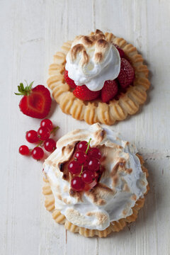 Two meringue tartlets with red currants and strawberries on wood, studio shot