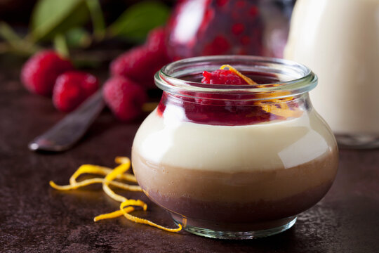Glass of pudding with vanilla sauce and raspberry sauce garnished with raspberries and orange zest